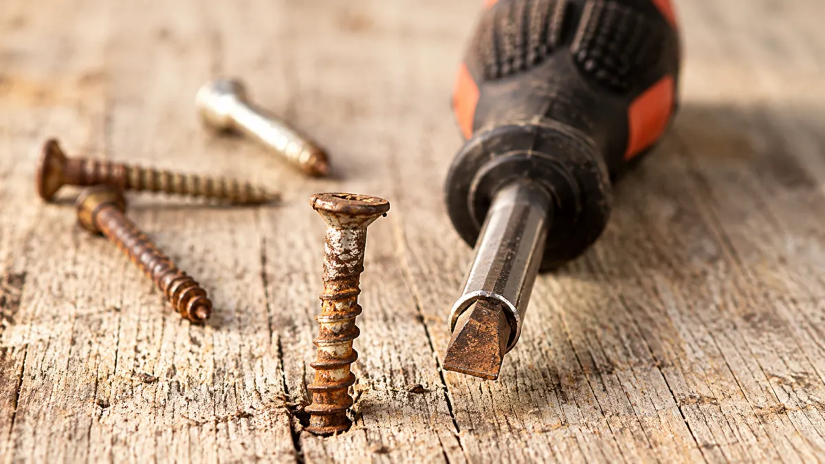 Rusty and stripped screws beside a screwdriver on a workbench.