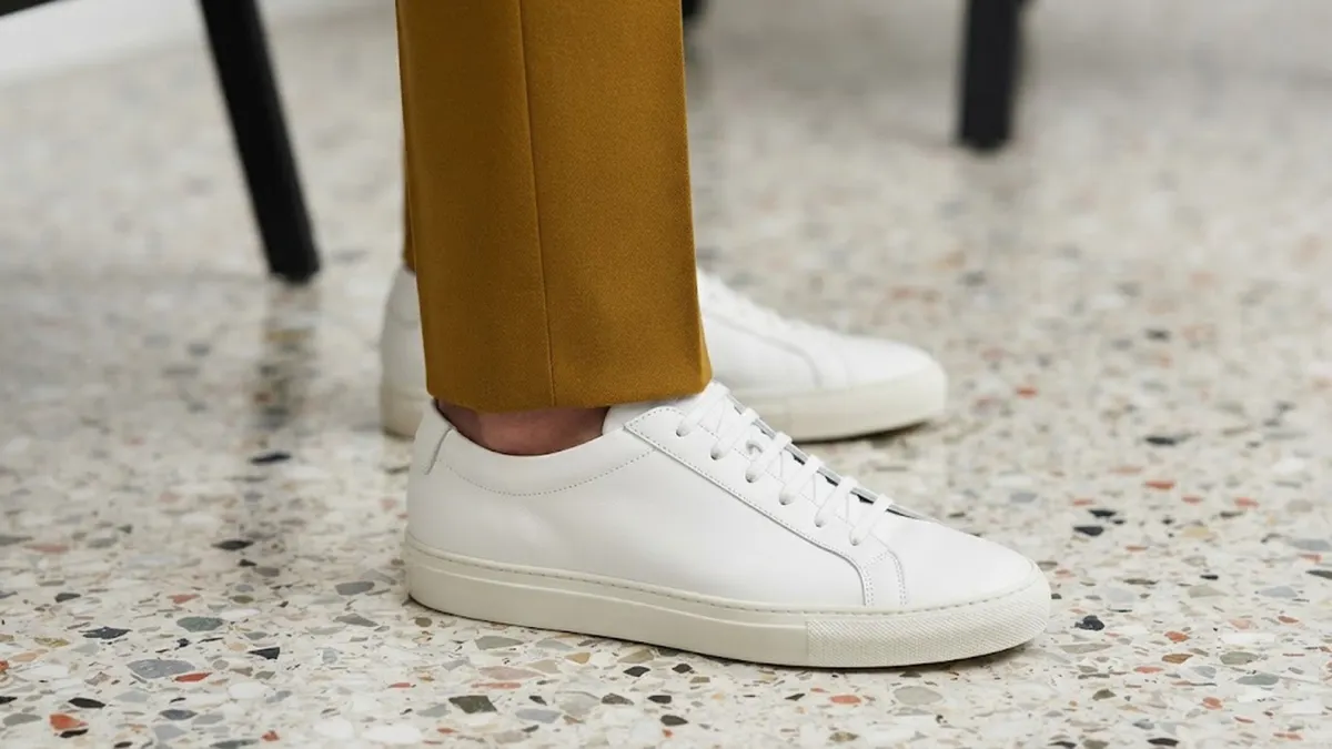 Mustard yellow pant hem resting over white sneakers